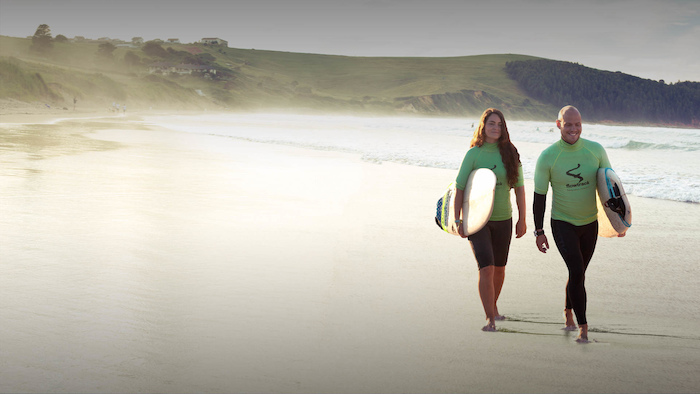 twee instructeurs lopen over strand met surfplank op surfkamp spanje