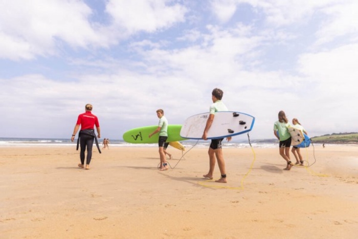 jongeren lopen richting de zee met surfplank onder arm op surfkamp spanje