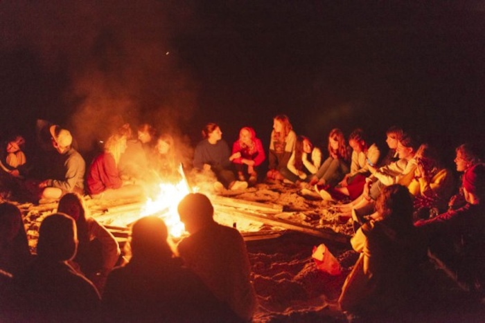 grote groep jongeren zit rondom kampvuur op surfkamp spanje