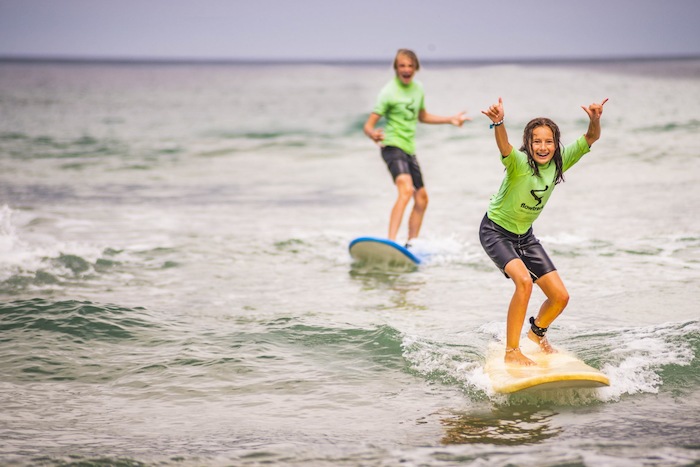 meisje doet surf symbool met handen terwijl ze op de surfplank staat 