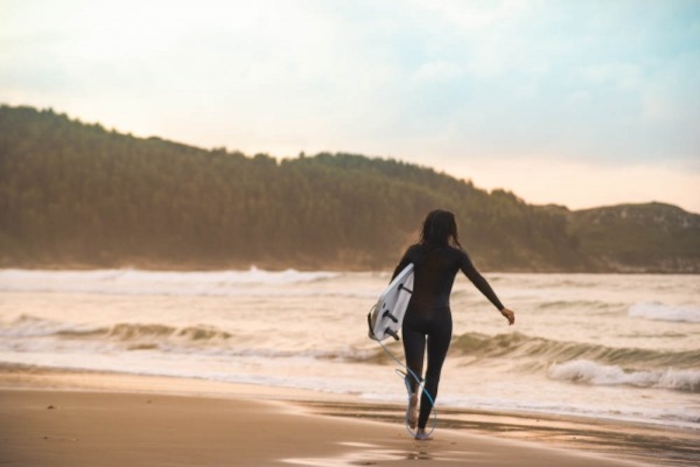 meisje met surfplank onder arm loopt langs de zee op surfkamp spanje