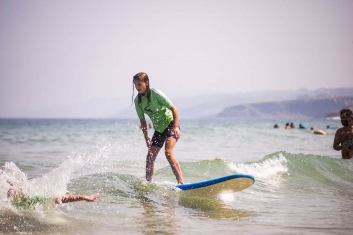 meisje op surfplank surft over golf en kijkt naar iemand in het water op surfkamp spanje