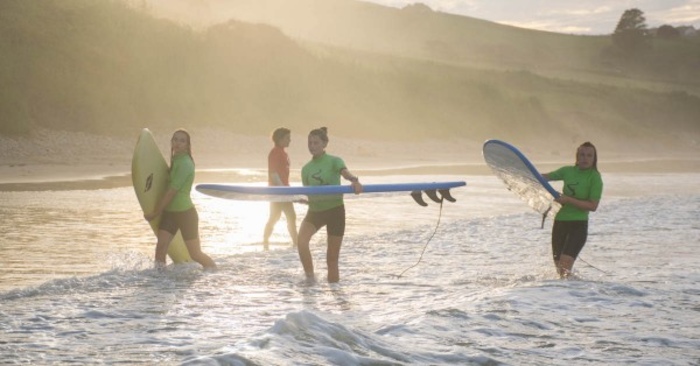 jongeren staan bij zonsondergang in de zee op surfkamp spanje