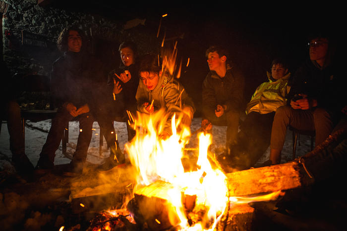 Deelnemers wintersportkamp zitten rond kampvuur, genieten van warmte