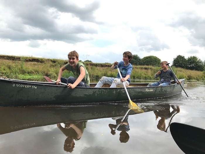 Jongens varen over rivier in kano en lachen op zomerkamp nederland.