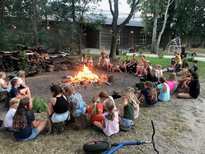 Kinderen zitten rond kampvuur in Overijssel op zomerkamp nederland