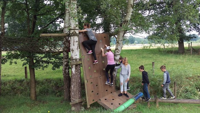 Kinderen klimmen over klimmuuur op survivalkamp in Overijssel op zomerkamp nederland