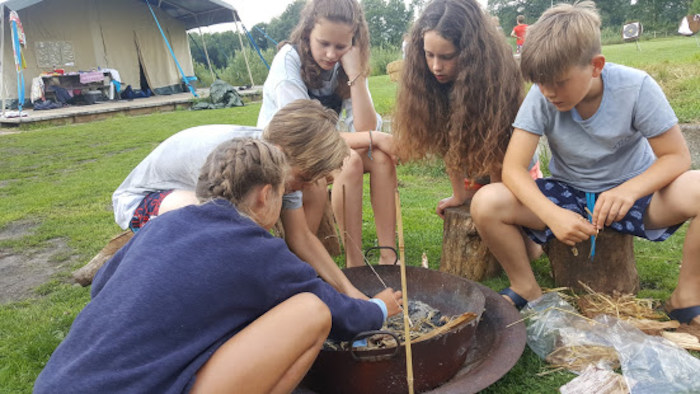 Meiden zitten rond kampvuur op survivalkamp in Overijssel op zomerkamp nederland