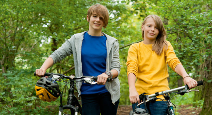 Twee meisjes wandelen door het bos met de fiets aan de hand