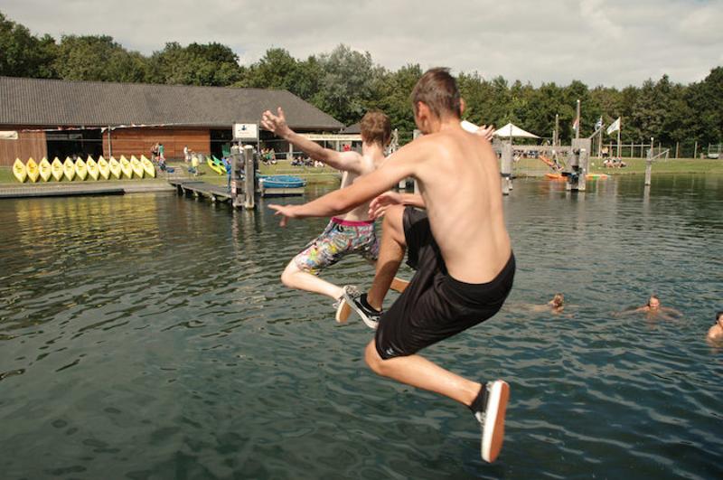 Tienerjongens springen in zomers water op kamp in Zeeland.