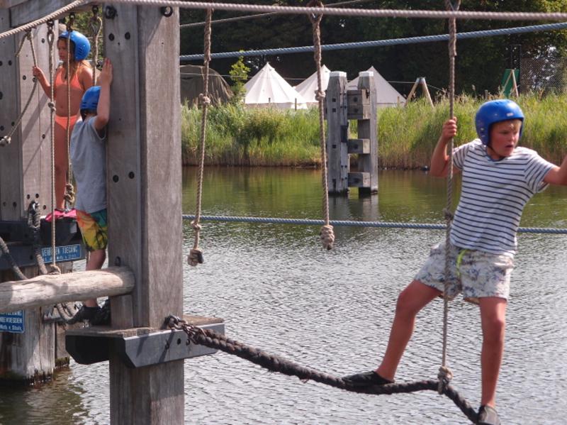Kinderen klimmen over touwen op zomerkamp in Zeeland.