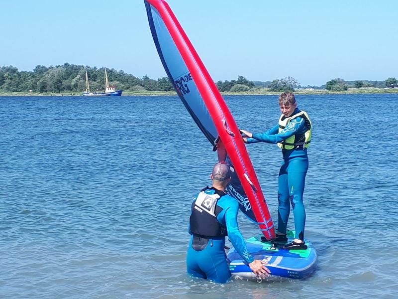 Begeleider helpt jongen windsurfen tijdens het zomerkamp in Zeeland.