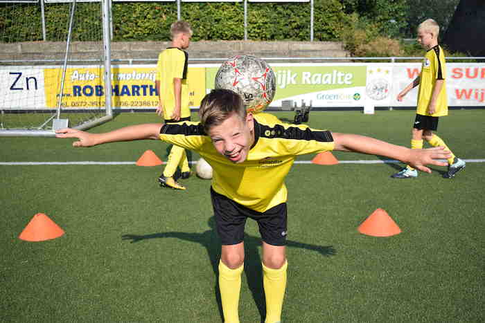 Jongen balanceert bal lachend op rug.