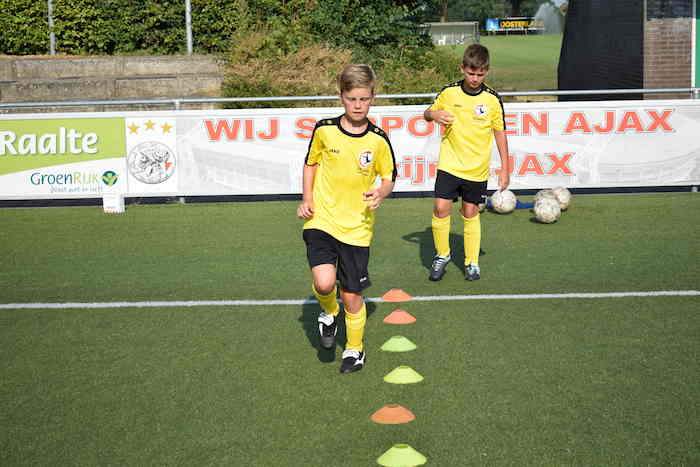 Jongens trainen voetbal op grasveld. 