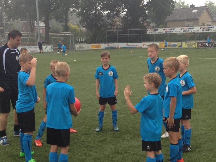 Jongen loopt lachend met trainer over voetbalveld.