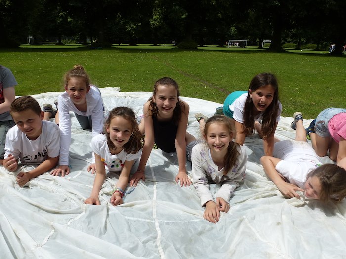 meisjes en jongen liggen op een witte parachute op de grond tijdens jeugdvakantie