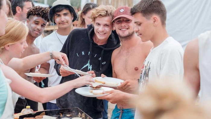 Jongeren houden bordjes vast met eten van de barbecue op surfkamp jongeren