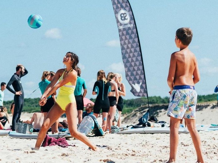 meisje slaat volleybal over net op het strand tijdens surfkamp voor jongeren in frankrijk