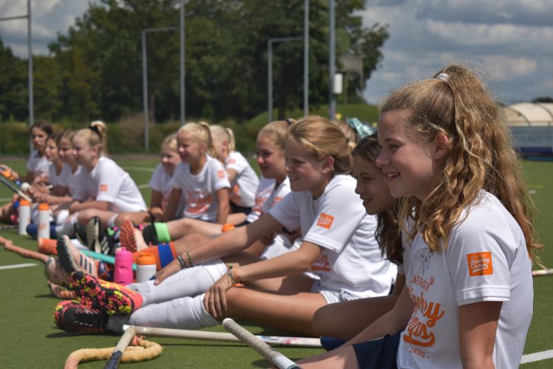 Een rij meiden zitten op het gras van een hockeyveld tijdens hen hockeykamp in Nederland