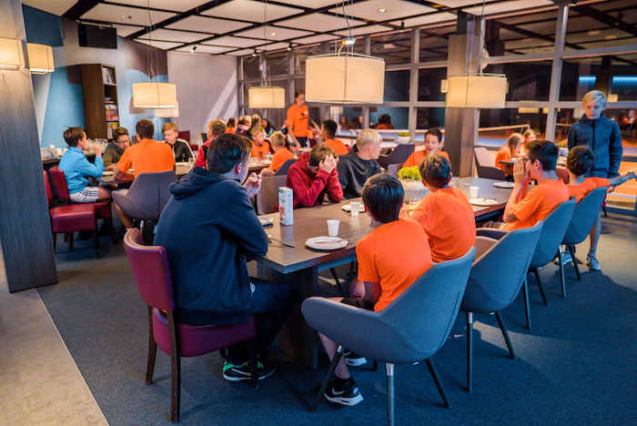 Jongeren eten samen in de eetzaal van de accommodatie op het tenniskamp in Brabant in de zomer.