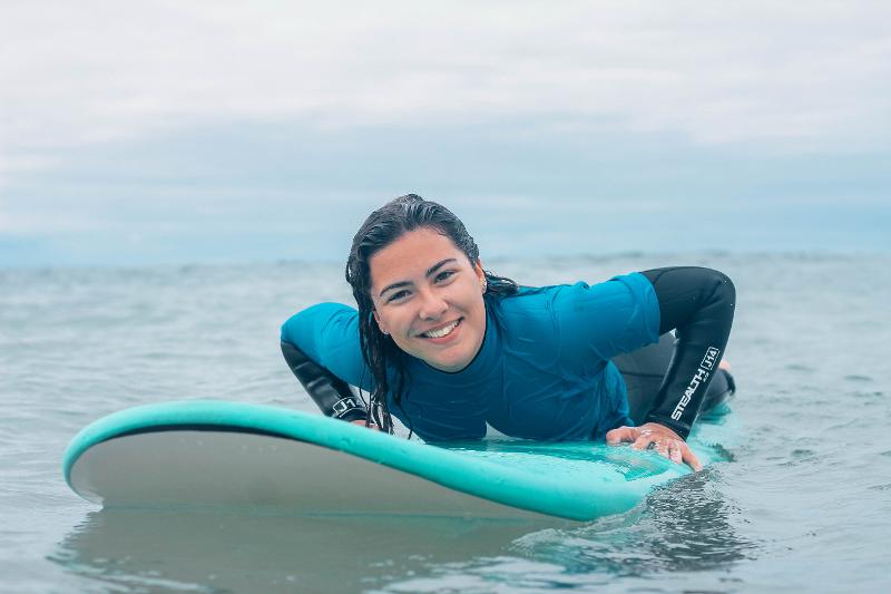 Een deelnemer aan een surfkamp in Portugal ligt op haar buik op een surfboard en lacht