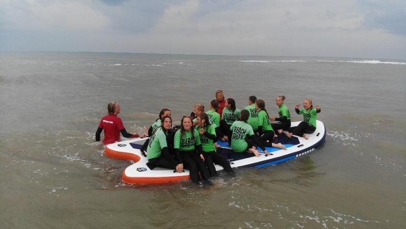 Groepje deelnemers zitten op een sup tijdens een surfkamp