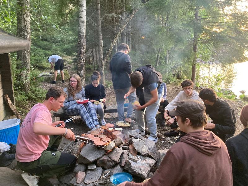 Een groep jongeren bakt hamburgers op een kampvuur tijdens een avonturenkamp