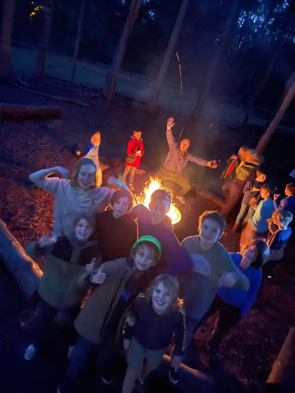 jongeren staan bij kampvuur in het donker op avonturenkamp belgië