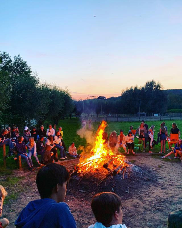 groep deelnemers zit rondom groot kampvuur in het donker op avonturenkamp ronse