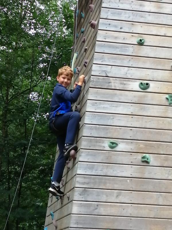 jongen klimt tegen muur en kijkt naar de camera op avonturenkamp ronse
