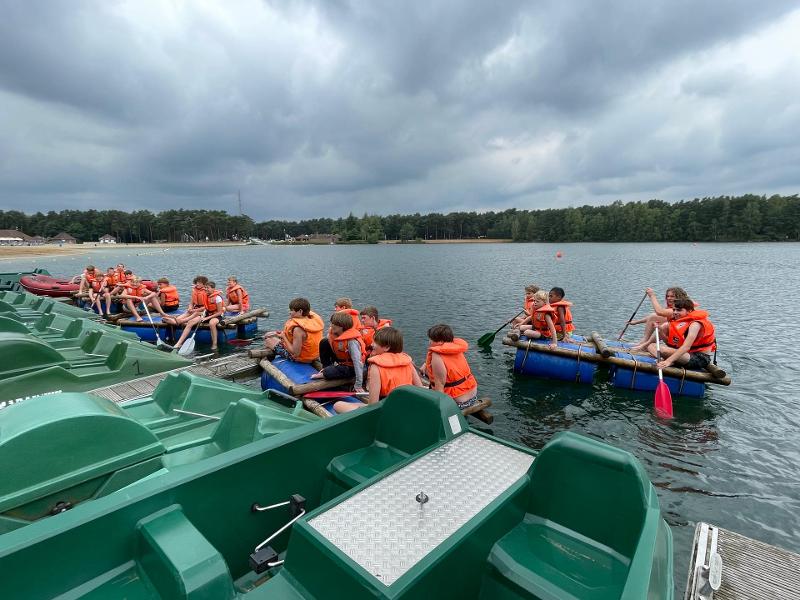 jongeren varen bij meer op zelfgebouwd vlot op outdoorkamp schoten
