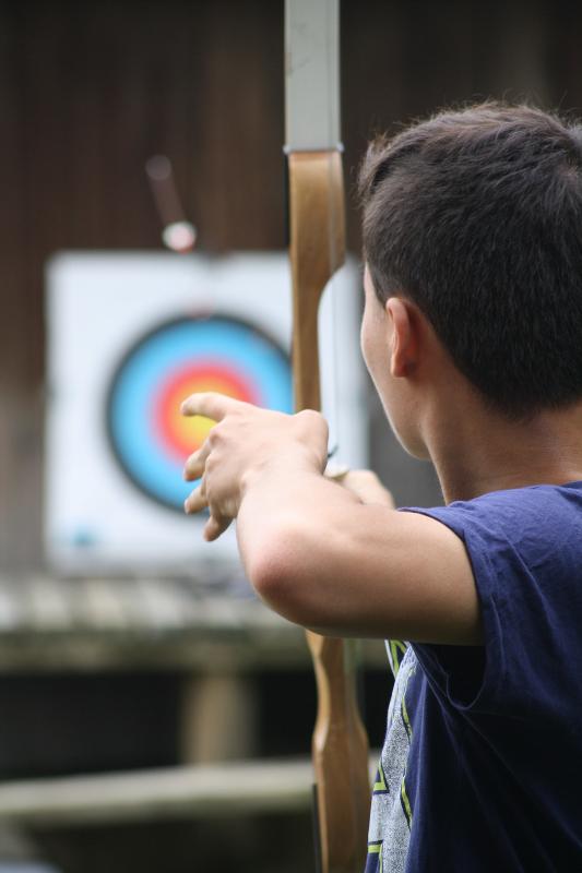 jongen richt met pijl en boog op doel op avonturen-gamekamp