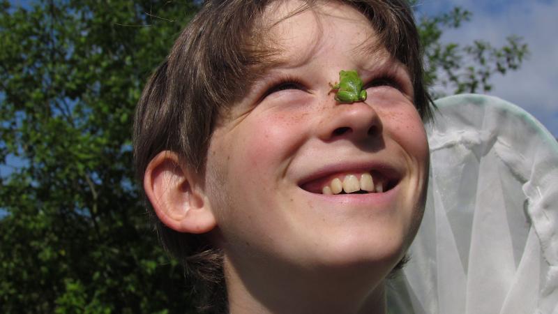 Jongen lacht en heeft een kikker op zijn neus tijdens een natuurkamp