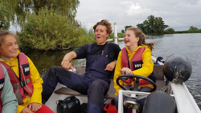 meisjes zitten bij jongen in boot op zeilkamp bij leiden