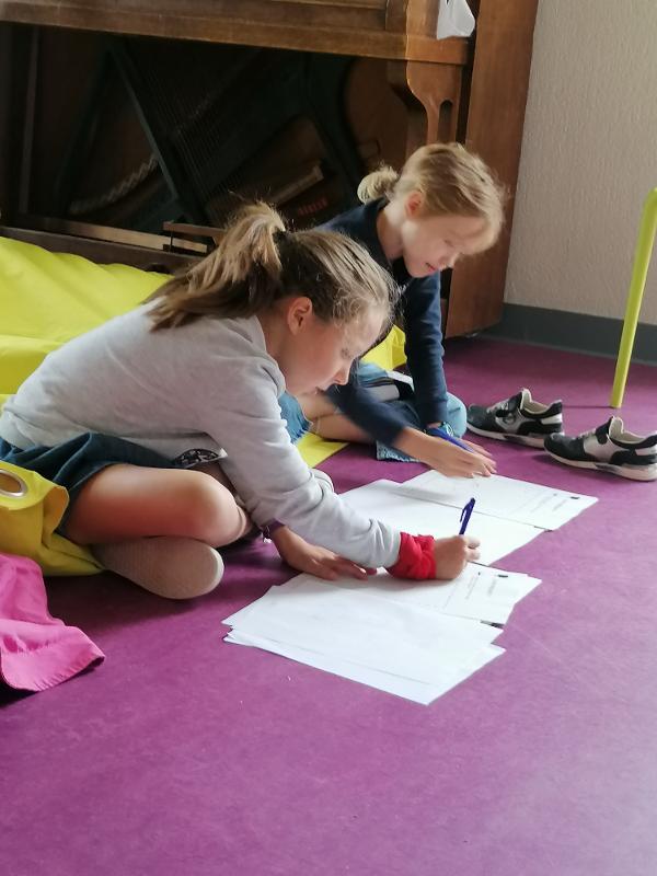 twee meisjes schrijven een script op de grond tijdens musical kamp