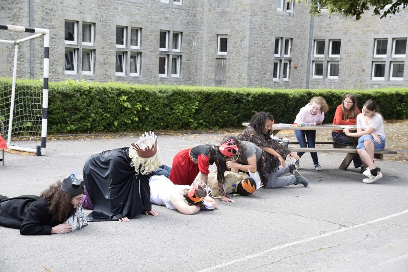 Een groep deelnemers aan musicalkamp België liggen op een schoolplein verkleed met kronen en capes