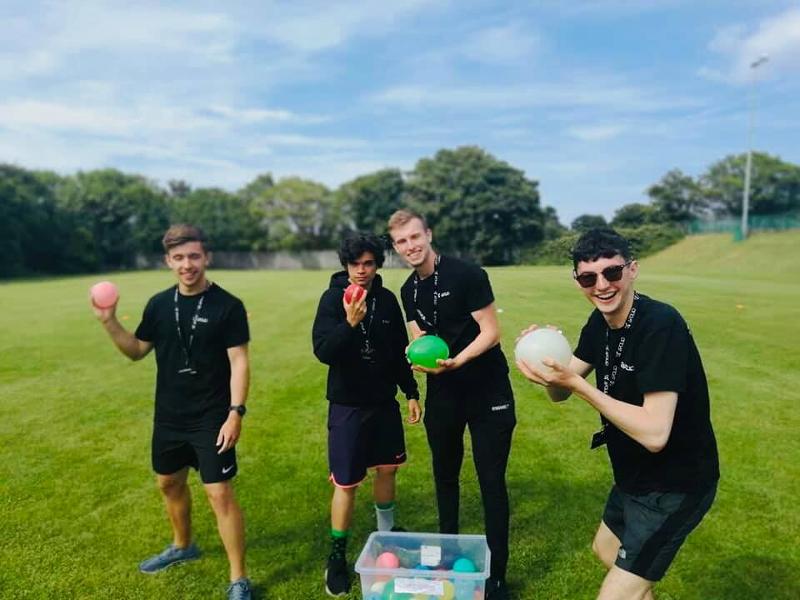 Vier jongens staan op een veld met waterballonnen tijdens een taalreis engels