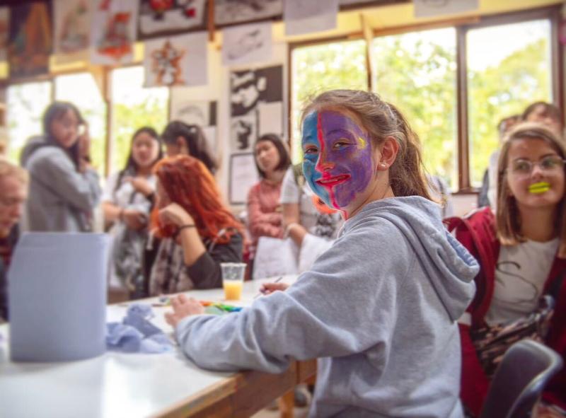 Een geschminkt meisje zit in een lokaal met andre meisjes tijdens een taalreis engels