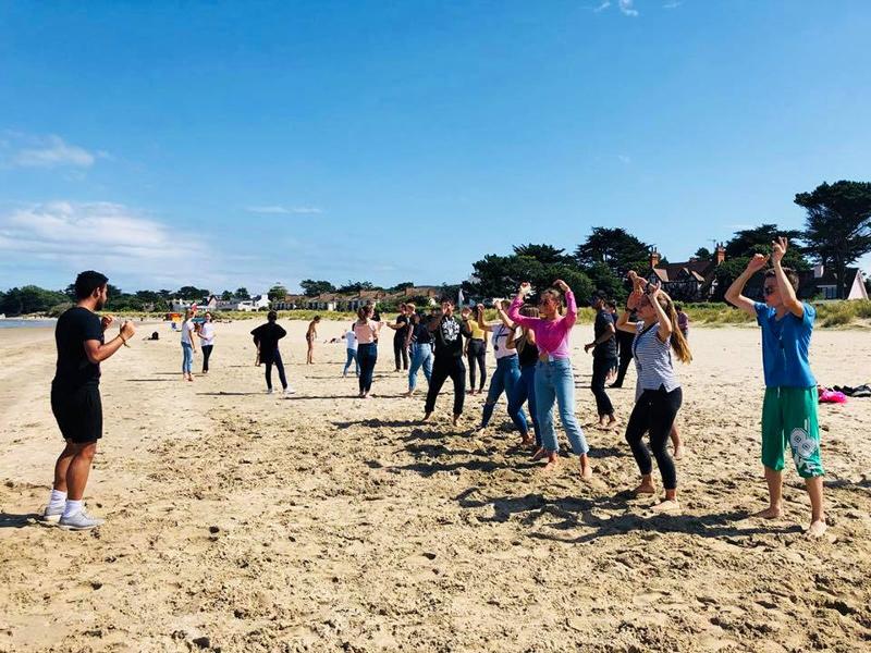 Jongeren doen gymnastiek oefeningen op het strand tijdens een taalreis engels