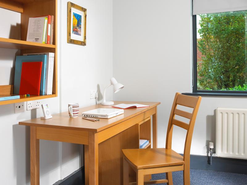 Een bureau, stoel en planken met boeken in een kamer tijdens een taalreis engels