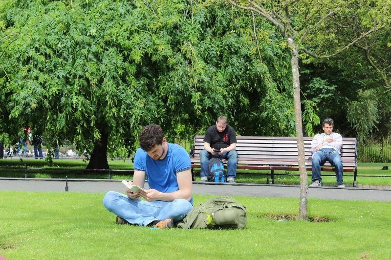 Mensen zitten op een bankje en in het gras in een park tijdens een taalreis engels