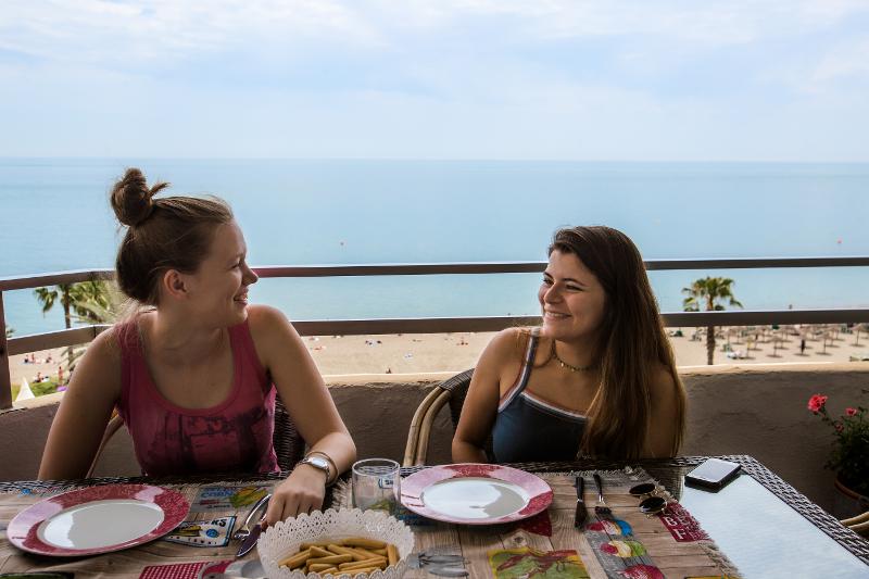 Twee meisjes eten ontbijt op een balkon met zeezicht tijdens een taalreis spaans