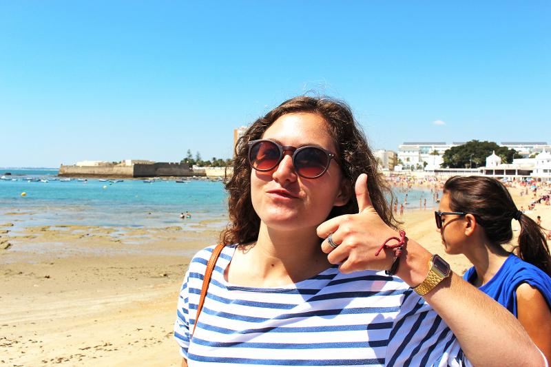 Een meisje poseert met haar duim omhoog voor de foto op een strand tijdens een taalreis spaans