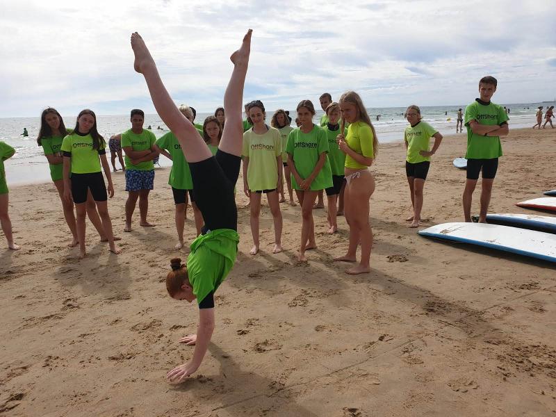 Een meisje doet een handstand op het strand met andere jongeren tijdens een taalreis spaans