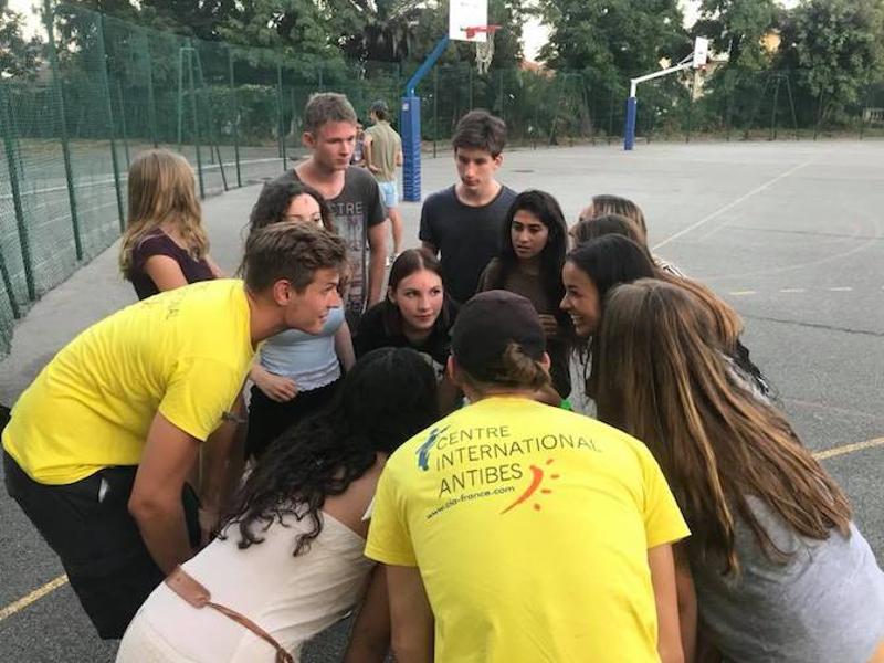 Jongeren en coaches staan bij elkaar in overleg op een basketbalveld tijdens een taalreis frans