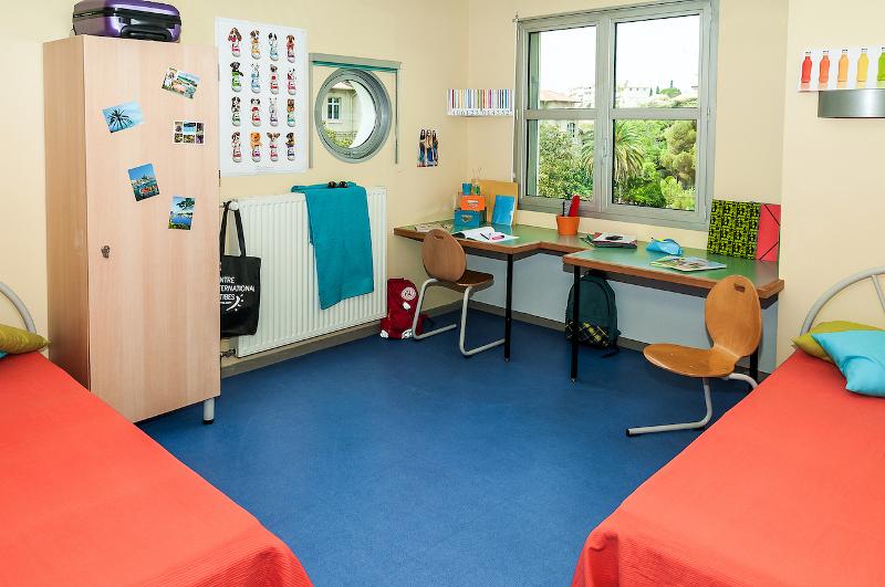 Een slaapkamer met twee bedden en bureaus en een kast tijdens een taalreis frans
