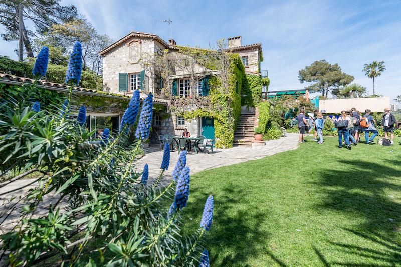 Een tuin met blauwe bloemen en een gebouw tijdens een taalreis frans