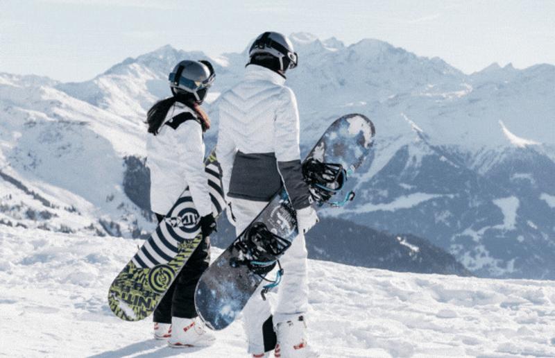 Deelnemers van jongeren groepsreis wintersport staan bovenop de berg te kijken naar berguitzicht met snowboards vast