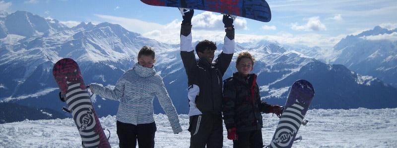 Deelnemers van de jongeren groepsreis wintersport staan op de berg op de foto met hun snowboards
