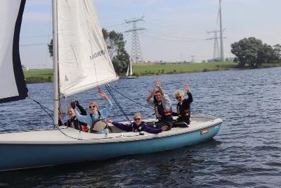 Deelnemers in zeilboot gooien handen in de lucht tijdens zeilkamp kinderen